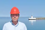 Man in blue shirt and red helmet in front of lighthouse