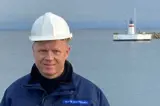Man in blue jacket and white helmet in front of lighthouse