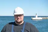 Man in black shirt and white helmet in front of lighthouse