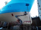 A ship undergoing a repainting of the hull to a light blue color