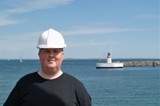 Man in black t-shirt and white helmet in front of lighthouse