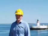 Man in blue shirt and yellow helmet in front of lighthouse